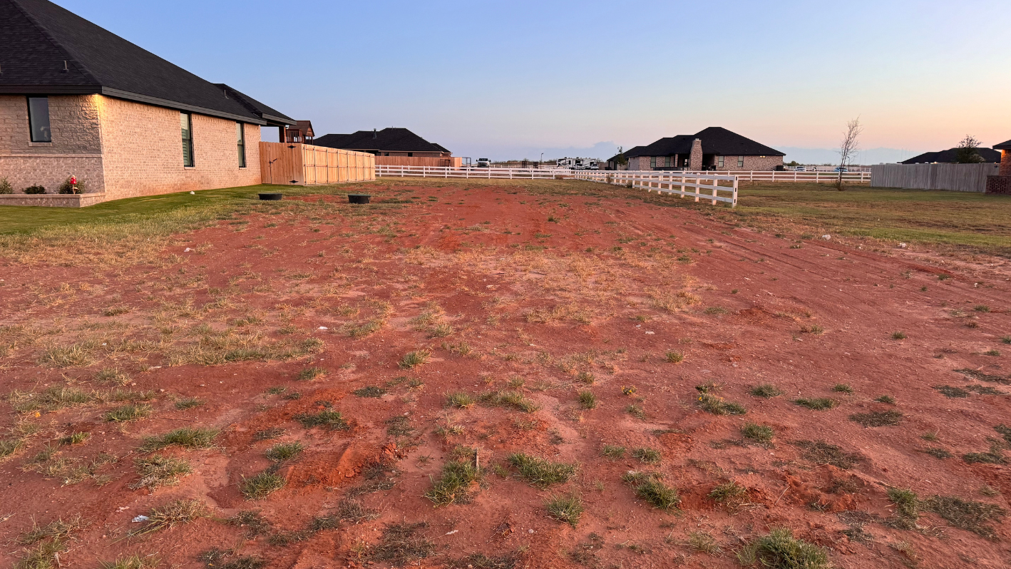 A dirt field with a house in the background